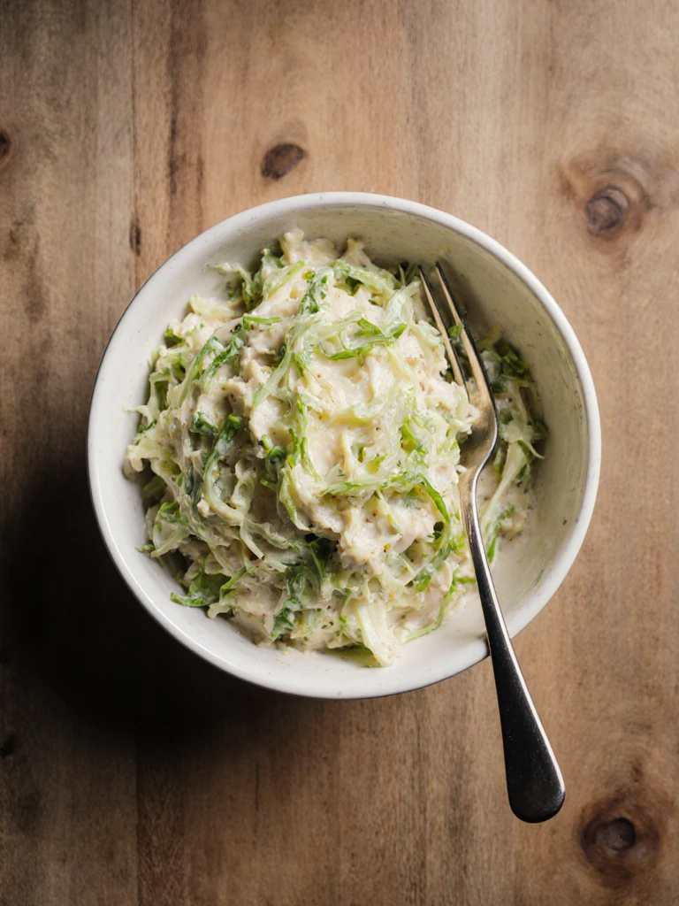 Apple cider vinegar coleslaw in a white bowl with celery seed and shredded green cabbage, overhead